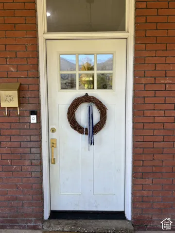 Brick exterior featuring a white paneled entry door with an upper window insert, brass hardware, and a brass mailbox
