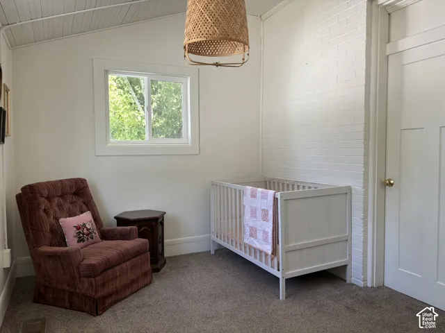 Vaulted ceiling with wood paneling, white painted brick accent wall, white trim window, and neutral carpeting