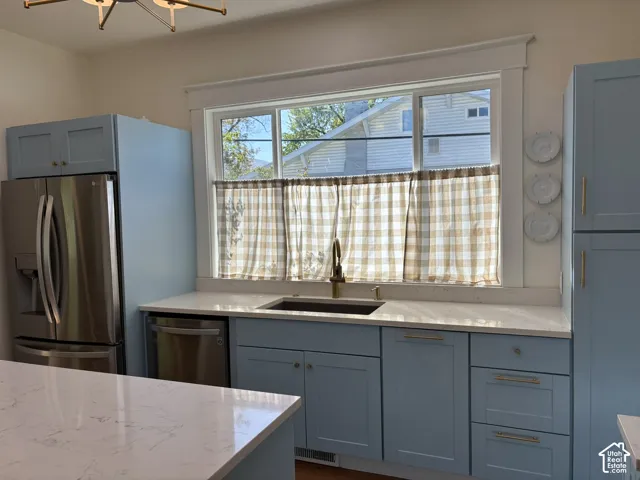 Kitchen featuring light blue cabinetry, light-toned countertops, a stainless steel refrigerator, and a stainless steel dishwasher