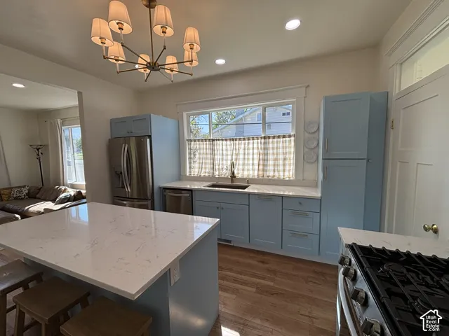 Kitchen featuring light blue cabinetry, stainless steel appliances, a white stone countertop, wood-finish flooring, and a contemporary chandelier