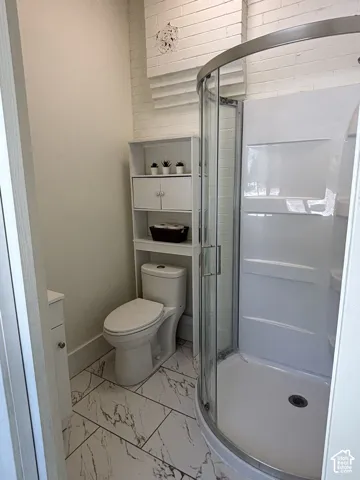 White brick accent wall with a curved glass-enclosed shower
