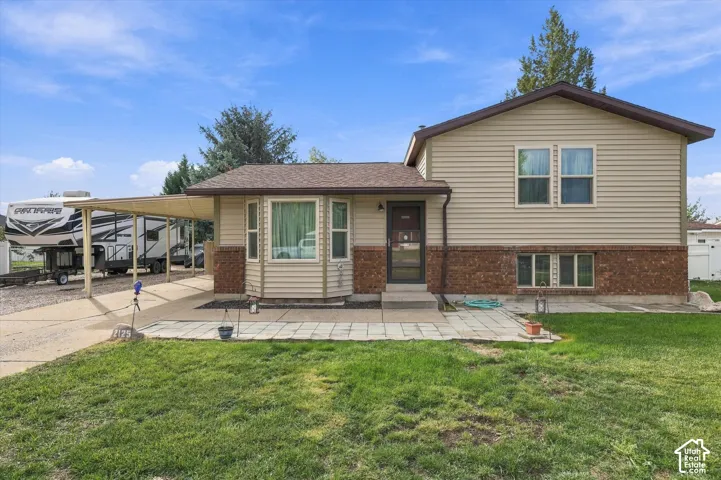 Split-level exterior featuring horizontal siding, masonry lower-level veneer, an integrated carport, a paved front patio, and a bay window
