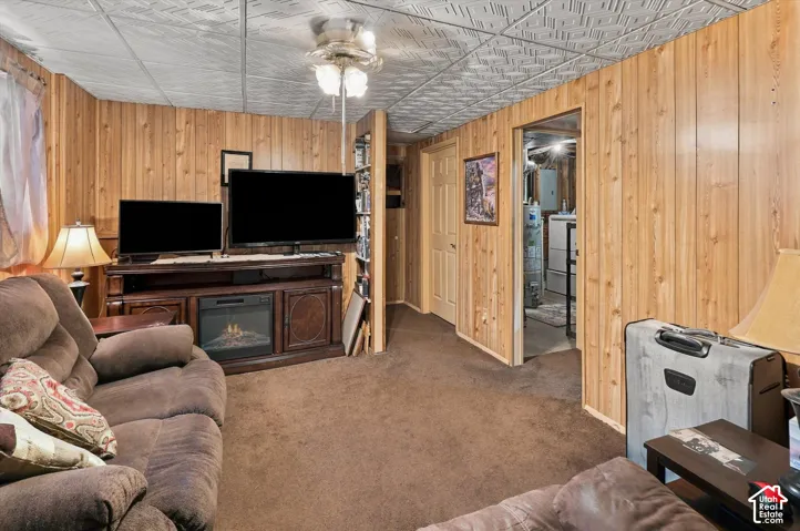 Interior room featuring wood-paneled walls, a ceiling with decorative tiles, a central light fixture with an integrated ceiling fan, and carpeted flooring
