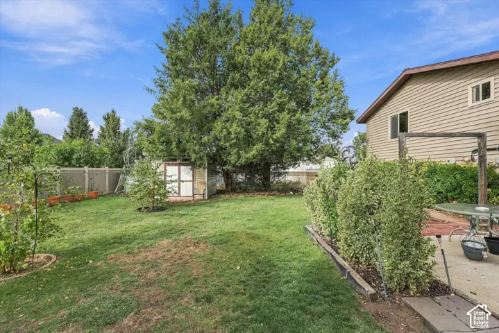 Backyard featuring a concrete patio, perimeter privacy fencing, mature trees, and a detached storage shed