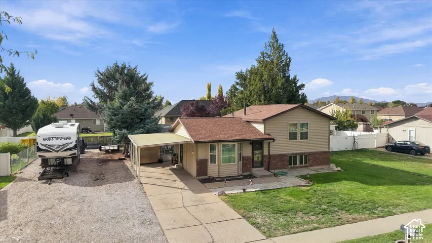 Split-level exterior featuring vinyl siding, brick accents, a covered carport, expansive gravel side parking, and a concrete patio