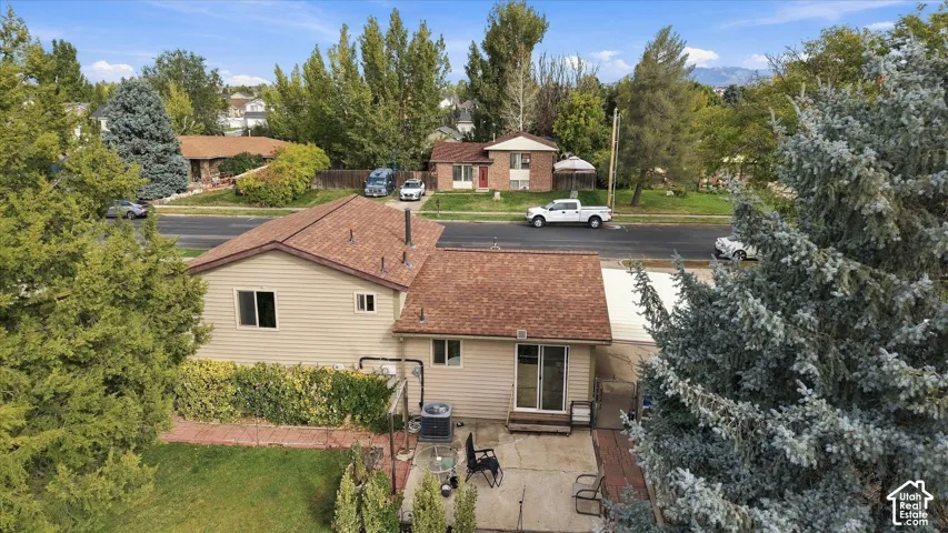 Exterior featuring light-tone horizontal siding, asphalt shingle roof, concrete patio, and mature landscaping