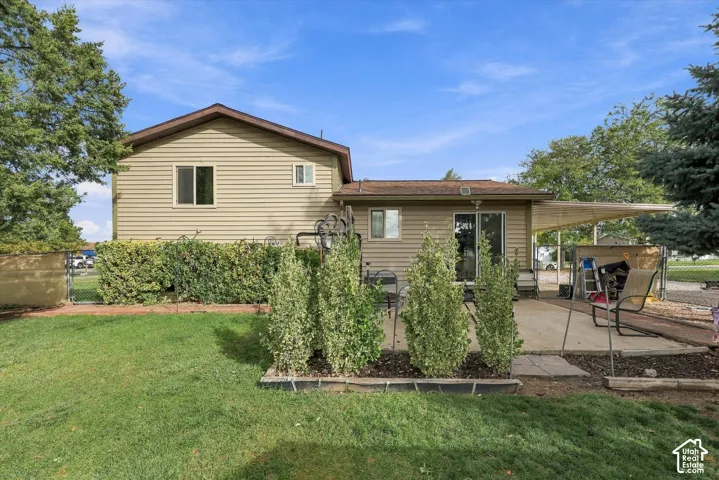 Rear exterior featuring horizontal vinyl siding, a covered patio, a manicured lawn, hedge landscaping, and a chain-link fenced perimeter