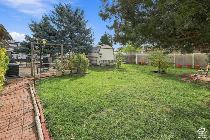 Backyard featuring a brick-paver pathway, mature evergreen trees, a detached storage structure, and perimeter privacy fencing