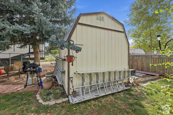 Exterior storage shed featuring a gambrel roof design, vertical siding, and perimeter chain-link fencing