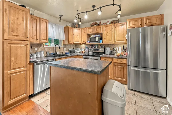 Kitchen featuring wood cabinetry, stone-finish countertops, stainless steel appliances, a center island, and track lighting