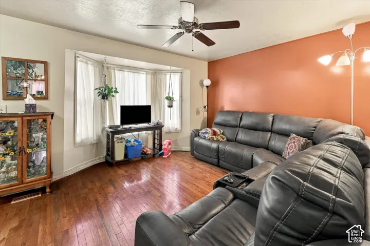 Living area featuring wood-finish flooring, a multi-paneled bay window, and a ceiling fan