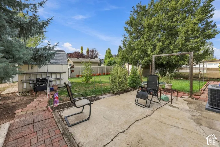 Backyard featuring a concrete patio, brick paver pathway, detached storage shed, and mature trees