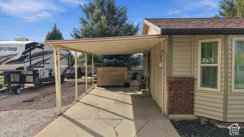Covered carport with concrete flooring, beige horizontal siding, and brick masonry foundation detailing