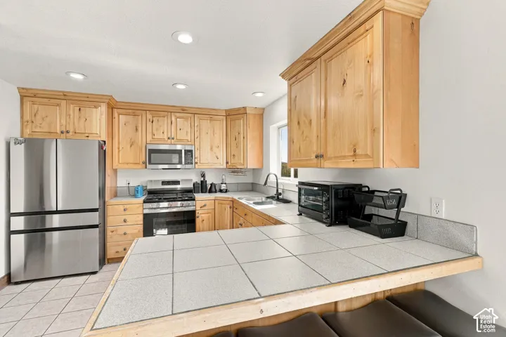 Kitchen featuring wood cabinetry, tiled countertops, stainless steel appliances, and recessed lighting