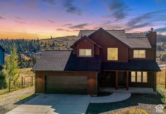 Multi-level residence featuring dark-toned exterior siding, a shingle roof, an attached two-car garage, and a covered front entry, set against a mountainous landscape