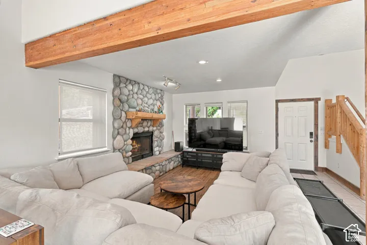 Living area featuring vaulted ceilings with exposed wood beams, river rock fireplace surround, stone hearth, and wood-finish flooring