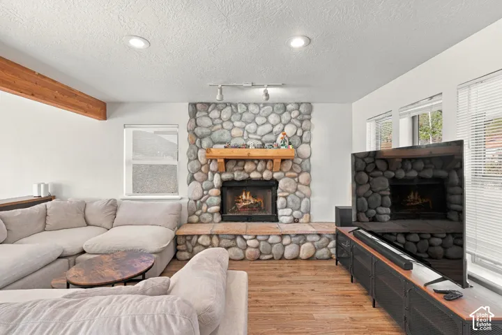 Floor-to-ceiling river rock fireplace with a wood mantel, stone hearth, wood-finish flooring, recessed lighting, and exposed ceiling beam