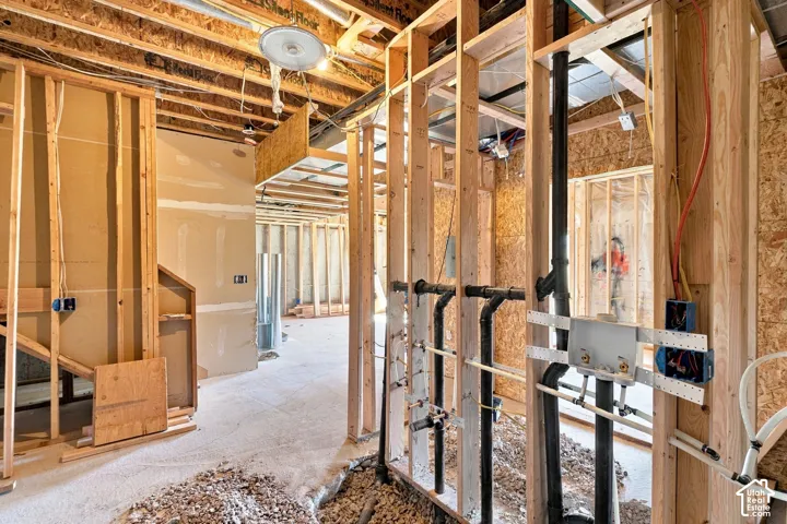Construction interior featuring exposed timber framing, visible plumbing infrastructure, electrical wiring, and drywall panels