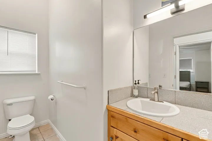 Bathroom featuring a vanity with a light-finish wood cabinet, a stone-tile countertop, an integrated oval basin, and a wall-mounted light fixture