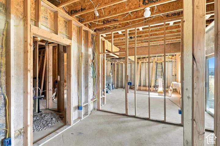 Structural framing in progress featuring exposed wood stud walls, open-joist ceiling construction, electrical wiring, and a concrete foundation