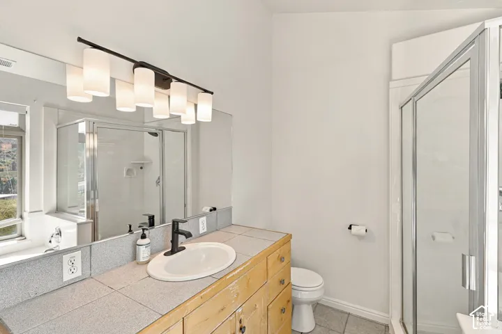 Bathroom featuring a vanity with tile countertop, undermount sink with matte black faucet, wall-to-wall mirror, six-light fixture, and glass-enclosed shower