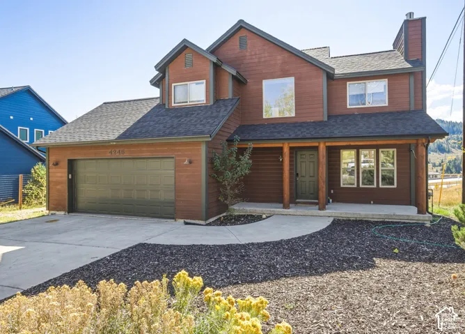 Two-story exterior featuring horizontal wood siding, a covered front porch with timber posts, an attached two-car garage, and a concrete driveway