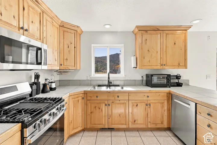 Kitchen featuring knotty wood cabinetry, stainless steel appliances, tiled countertops, recessed lighting, and mountain scenery