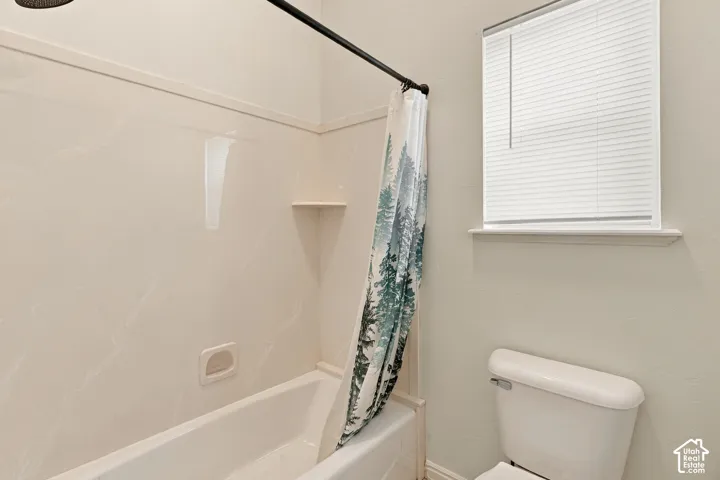 Tub and shower combination featuring smooth wall surround, integrated shelving, and a dual-handle fixture, paired with a window and a standard-height toilet