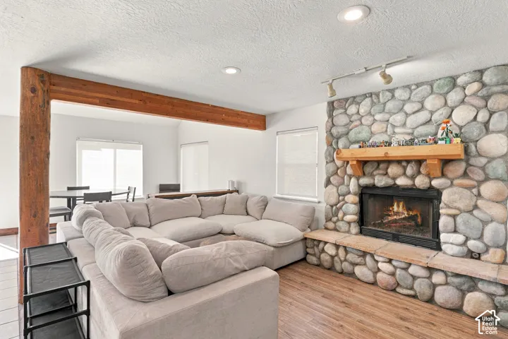 Full-height river rock fireplace featuring a wood mantel and raised hearth, exposed timber beam, wood-finish flooring, and recessed lighting