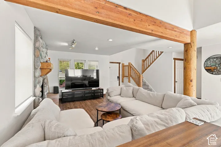 Vaulted ceiling featuring exposed timber beams, natural stone masonry fireplace, and wood-finish flooring