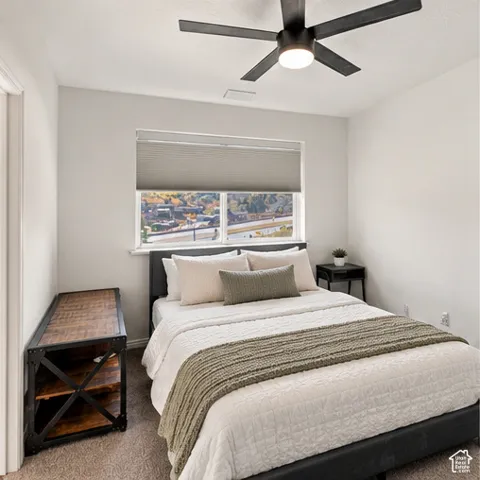 Neutral-toned carpeted flooring, large window with integrated blind, matte black four-blade ceiling fan with central light fixture, and textured wall finish