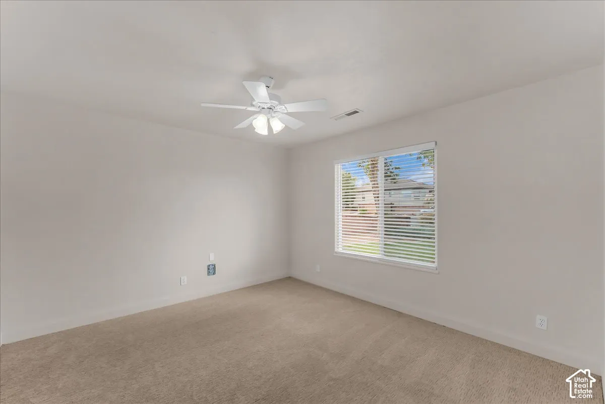 Neutral-toned interior featuring wall-to-wall carpeting, a multi-blade ceiling fan with integrated lighting, and a window with horizontal blinds