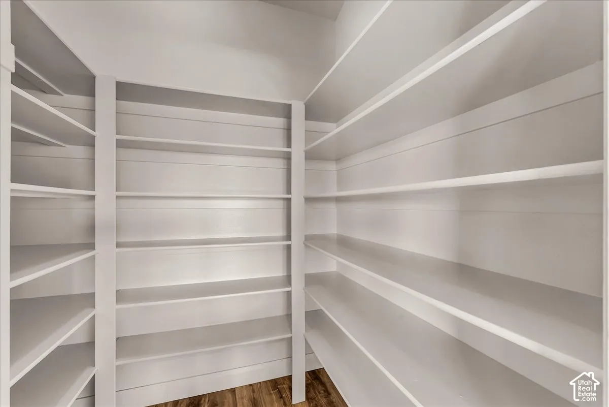 Walk-in storage area featuring floor-to-ceiling white shelving, horizontal wall paneling, and wood-finish flooring