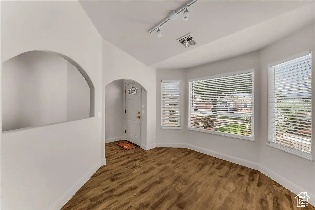 Wood-finish flooring, recessed wall niche, vaulted ceiling, track lighting, and bay windows