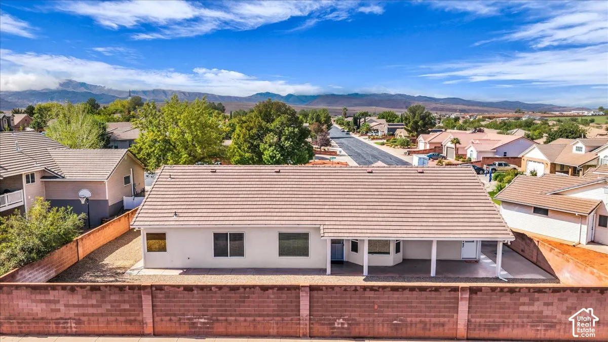 Single-level residence featuring a tile roof, covered patio, and concrete block perimeter wall, situated against a mountain backdrop