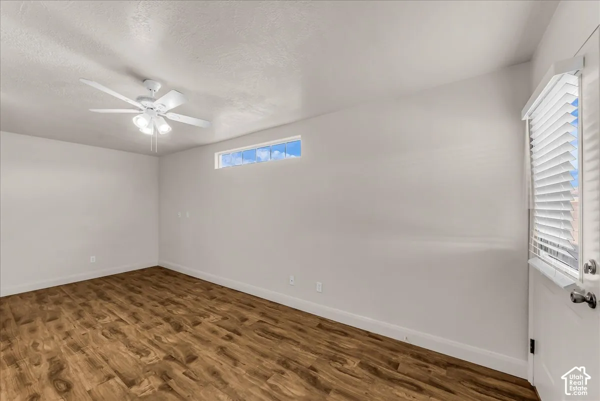 Room featuring wood-finish flooring, a white ceiling fan with integrated lighting, a horizontal transom window, and a door with an inset window
