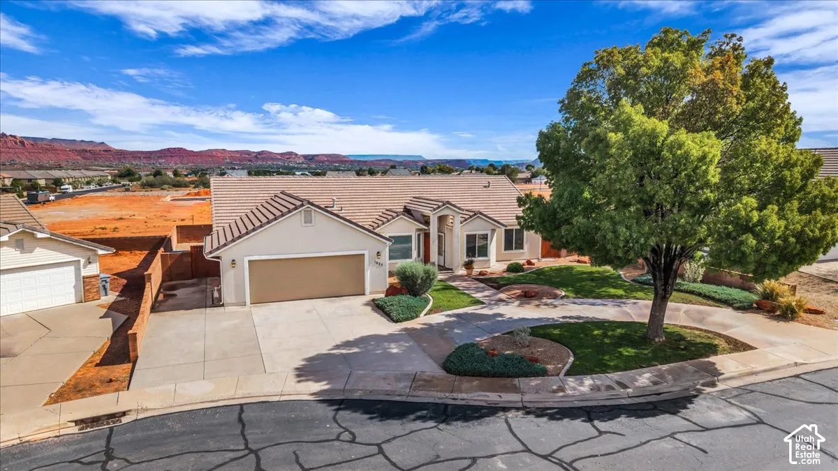 Single-story residence featuring a tile roof, stucco exterior, attached multi-car garage, concrete driveway, and mature landscaping