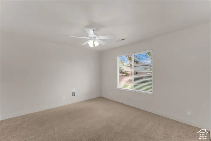 Neutral-toned interior featuring wall-to-wall carpeting, a multi-blade ceiling fan with integrated lighting, and a window with horizontal blinds