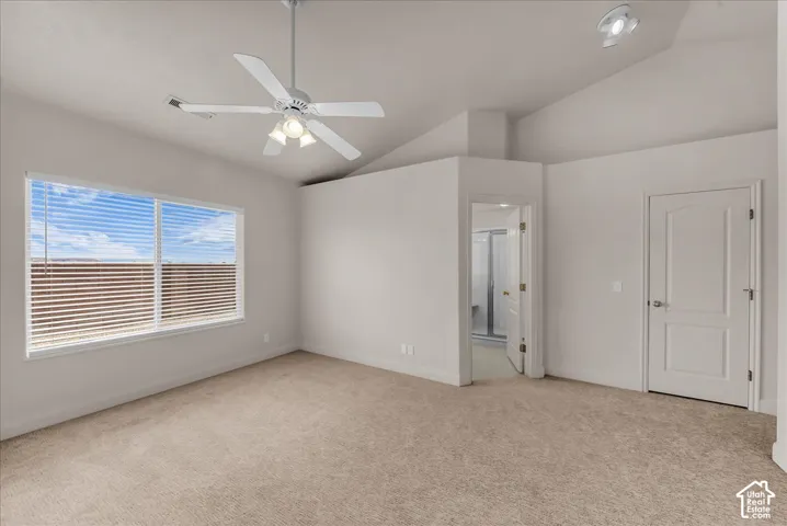 Vaulted ceilings featuring a white ceiling fan with integrated lighting, neutral wall-to-wall carpeting, and a dual-panel interior door
