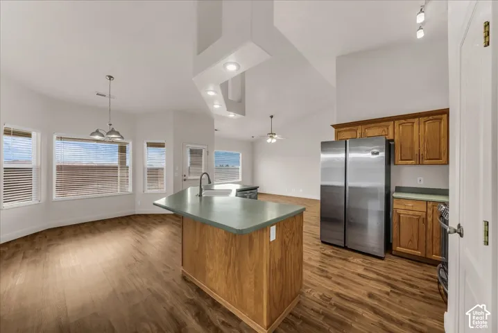 Kitchen featuring wood cabinetry, solid-surface countertops, wood-finish flooring, vaulted ceilings, and stainless steel side-by-side refrigerator