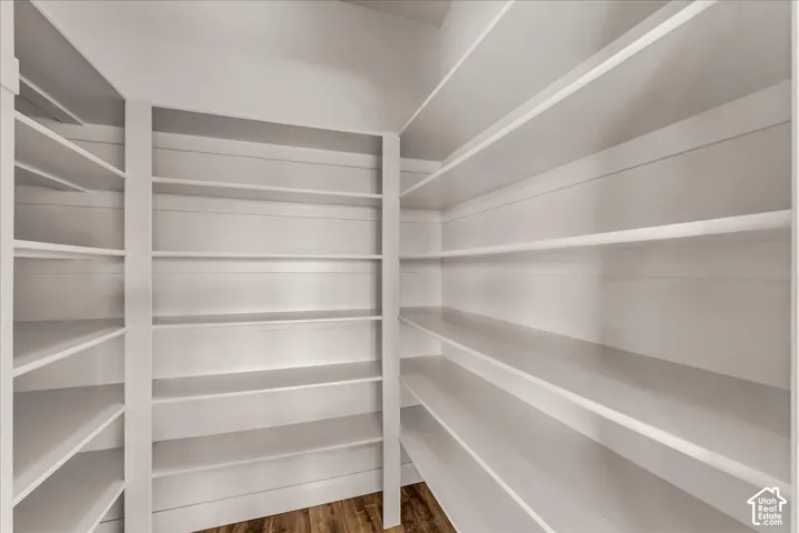 Walk-in storage area featuring floor-to-ceiling white shelving, horizontal wall paneling, and wood-finish flooring