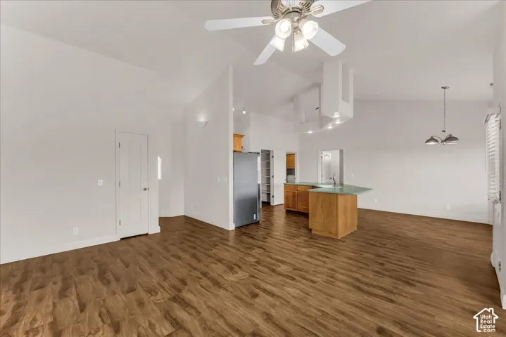 Vaulted ceilings, wood-finish flooring, kitchen island with countertop, overhead ceiling fan with light fixture, and pendant lighting