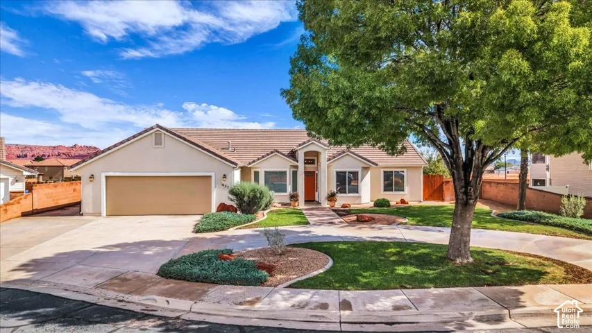Single-story residence featuring a neutral stucco exterior, a tile roof, an attached two-car garage, and a landscaped front yard with a mature shade tree