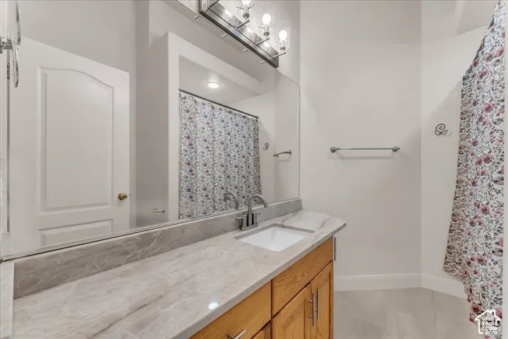 Bathroom vanity featuring a natural stone-finish countertop, undermount sink, warm-toned wood cabinetry, wall-to-wall mirror, and multi-bulb light fixture
