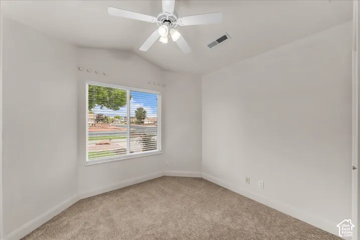 Room featuring vaulted ceilings, neutral wall tones, wall-to-wall carpeting, a multi-blade ceiling fan with integrated lighting, and a single window with horizontal blinds