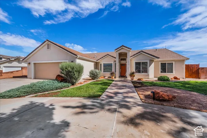 Single-story exterior featuring a stucco finish, multi-gable roofline, attached multi-car garage, concrete driveway, and xeriscaped front yard with mature shrubs
