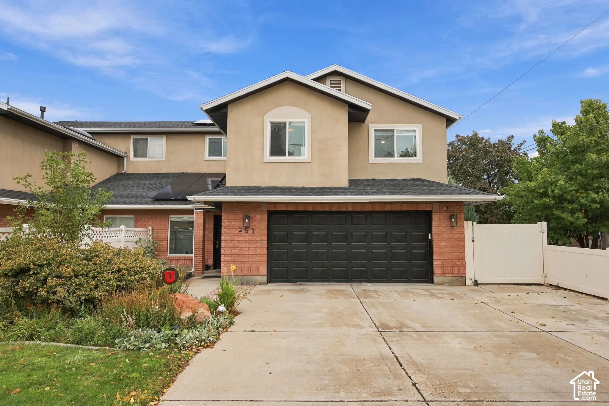 Multi-level exterior featuring a brick and stucco facade, a two-car garage, roof-mounted solar panels, and gated side access
