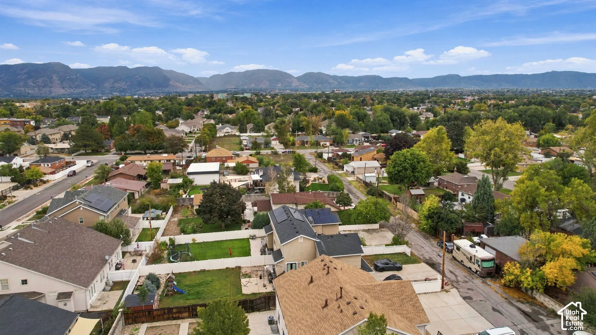Aerial perspective of a residential neighborhood featuring established trees, manicured lawns, asphalt roads, and a prominent mountain range backdrop