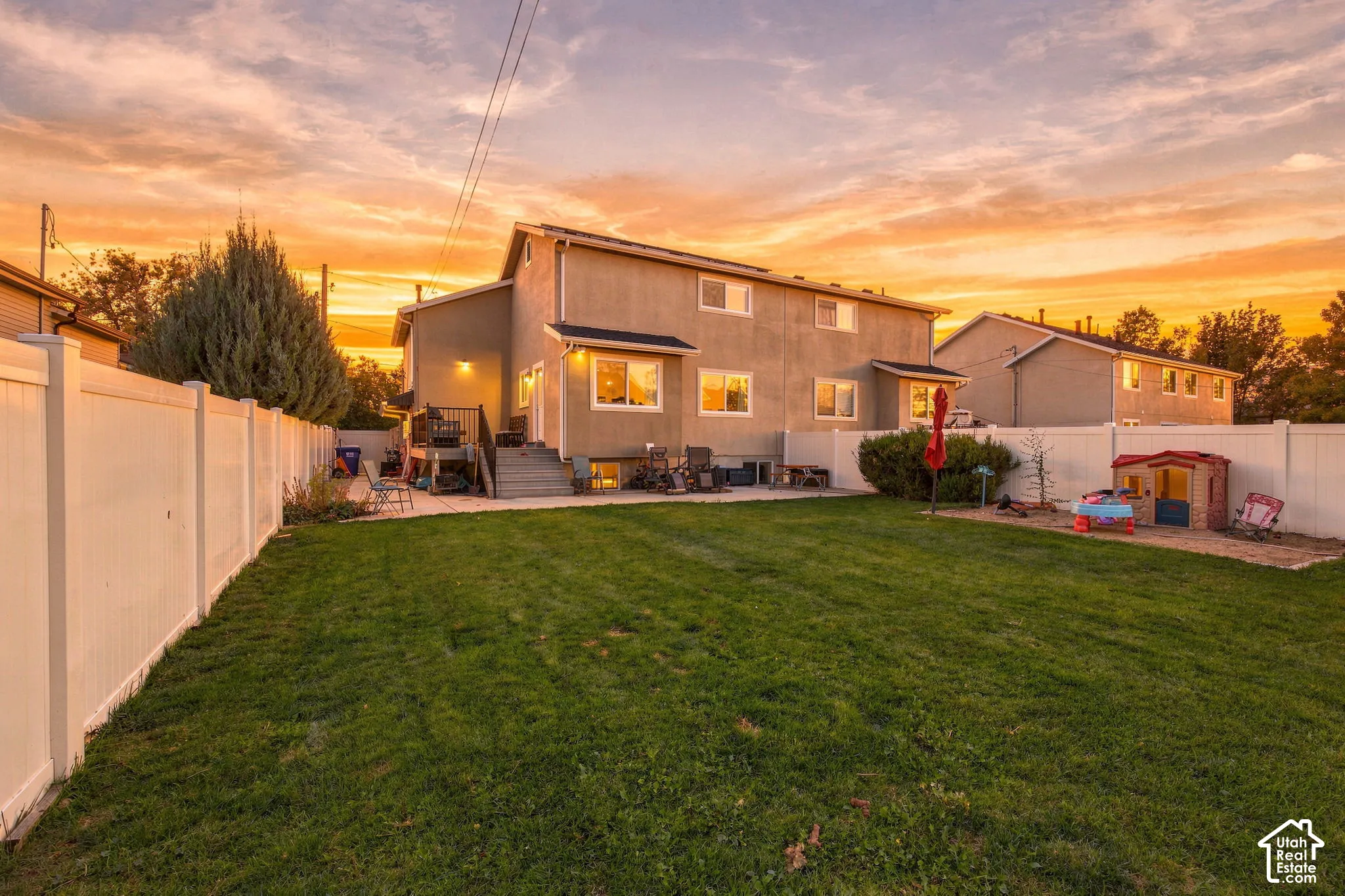 Rear exterior featuring a manicured lawn, full-perimeter white vinyl fencing, concrete patio, and elevated wood-finish rear deck