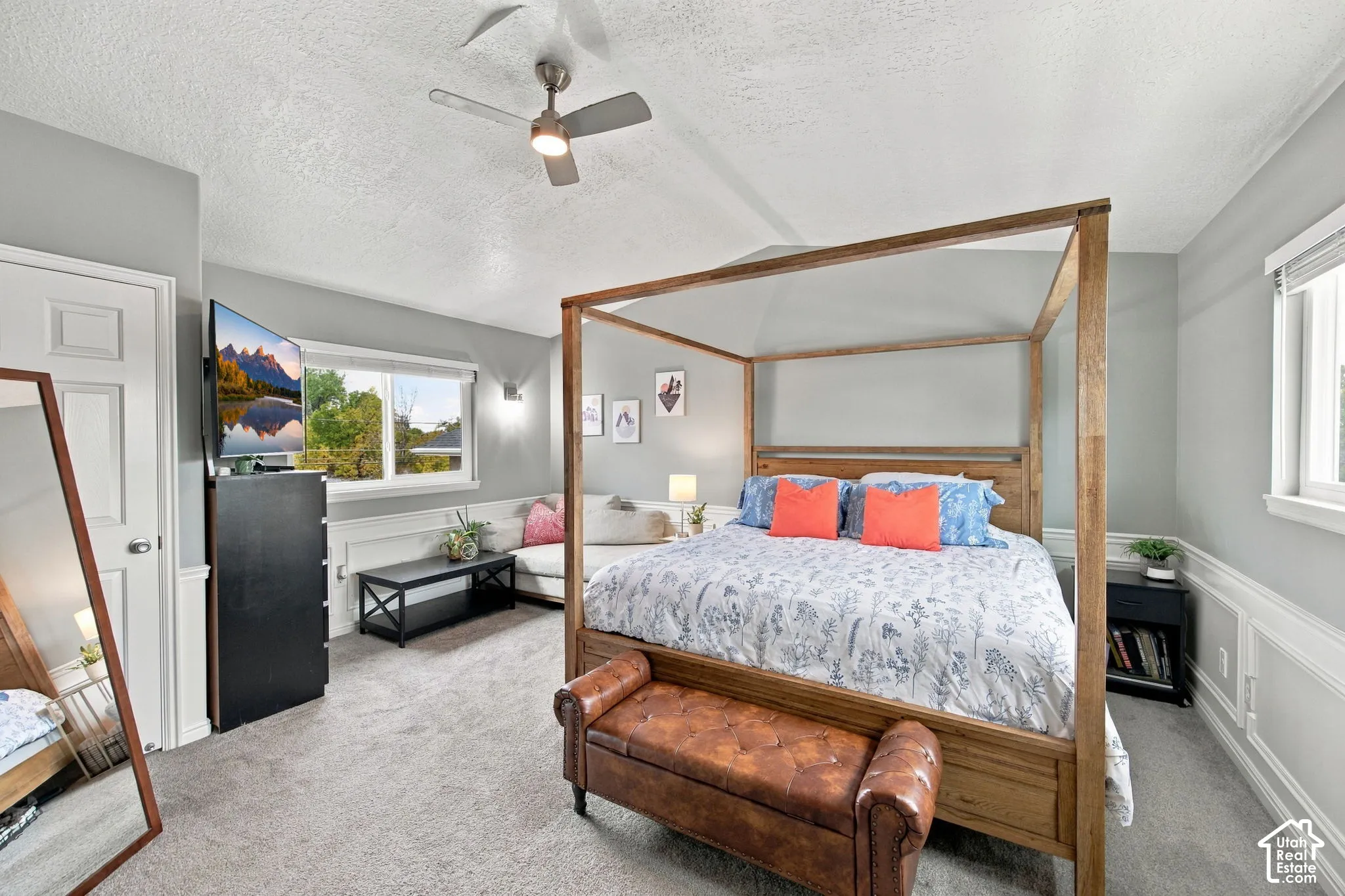 Vaulted ceiling with a central brushed-metal ceiling fan, neutral wall-to-wall carpeting, and wainscoting detailing along the lower perimeter walls